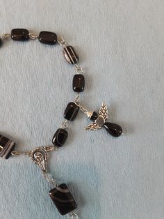 Banded Black Agate Stone Pocket Rosary, Banded Blackagate stones 18mm x 13mm and 12mm x 8mm, Silver alloy Maria Connector 18mm x 16mm and Crucifix 55.5mm x 34mm. Angel is black Stone Beads 27mm x 27mm wing span All beads are hand chained togetherusing High quality 20ga silver plated copper wire Wire, Rosaries come in a Royal Blue Velvet drawstring pouch.  I have been designing and making jewelry and Rosaries for approximately 15 years. I truly enjoy the design and making aspect. Originally I began making for personal use, I was soon overrun with more jewelry than one person can wear. My employer had a yearly campaign for Breast Cancer Awareness and Children's Miracle Network Hospitals. In making pieces that could be sold as a means to raise money for these Charitable Organizations,  I was Black Oval Beads Jewelry For Gift, Black Oval Beaded Jewelry Gift, Black Oval Beaded Jewelry As Gift, Black Jewelry With Oval Beads As A Gift, Handmade Black Jewelry For Memorial, Black Natural Stone Oval Beaded Jewelry, Black Jewelry With Oval Natural Stones, Black Onyx Rosary As A Gift, Children's Miracle Network Hospitals