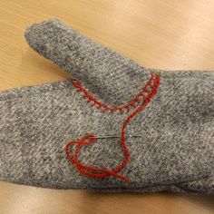 a pair of gray mitts with red thread on them sitting on a wooden table