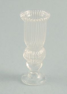 a clear glass vase sitting on top of a white tableclothed floor next to a gray wall