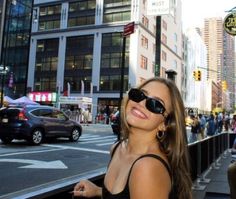 a woman wearing sunglasses standing on the side of a street