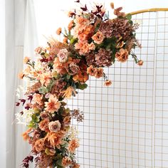 an arrangement of flowers is hanging on the side of a white wall in front of a window