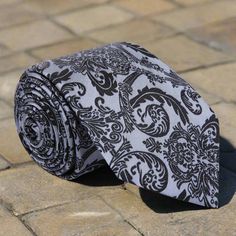 Elevate Your Style with Grey Silk Necktie Adorned with Intricate Black Floral Pattern Immerse yourself in sophisticated elegance with our captivating grey silk necktie embellished with an intricate black floral pattern. Discover the versatility and refinement this accessory brings to your wardrobe, offering timeless charm for various occasions. 1. The Elegance of Grey with Black Florals: This silk necktie exudes sophistication with its grey backdrop and finely detailed black floral pattern. The Classic Gray Tie For Wedding, Gray Wedding Tie, Elegant Fitted Silver Suit And Tie Accessories, Elegant Black Neckwear With Inside Ties, Elegant Black Neckwear For Gift, Elegant Gray Business Tie, Elegant Silver Suit And Tie Accessories For Party, Elegant Gray Suit And Tie Accessories For Formal Occasions, Silver Party Tie