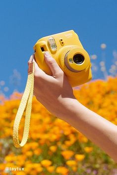 a person holding up a yellow camera in front of flowers