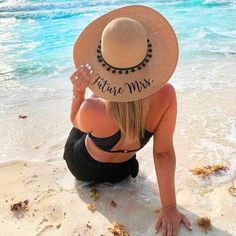 a woman sitting on the beach wearing a hat and looking out at the ocean from behind her