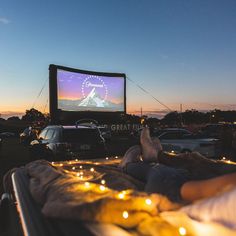 people sitting in the grass watching a movie at night with candles lit up around them