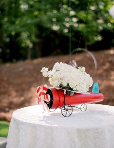 a table topped with a vase filled with white flowers and a red toy car sitting on top of it