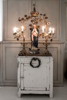 an old cabinet with candles and a statue on top in front of the wall behind it