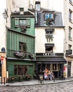 people are sitting at tables in front of a building on a cobblestone street