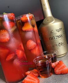 two tall glasses filled with liquid and strawberries next to a bottle of booze