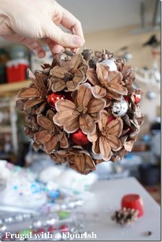 a person holding a pine cone ornament with christmas decorations on it and other items in the background