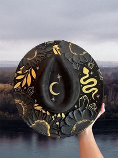 Halloween hat Brim is about 3.75" wide  Content: Vegan Suede Adjustable to fit your head better if needed  Elevate your style with this stunning hand-painted wide-brim fedora, crafted from luxurious vegan suede in a timeless black and gold palette. This one-of-a-kind piece is adorned with intricate designs featuring a serpent winding gracefully around the crown, sparkling crystals, celestial stars, delicate leaves, and a crescent moon. Each flower is meticulously painted with thick, textured strokes, adding a unique tactile dimension to the hat's sophisticated design. This fedora isn't just a hat; it's a wearable work of art. Perfect for making a statement at festivals, special events, or just adding a touch of magic to your everyday outfits. Whether you're dressing up or down, this versat Adjustable Flat Brim Halloween Costume Hat, Adjustable Flat Brim Halloween Hat, Adjustable Flat Brim Hat For Halloween, Custom Handmade Black Felt Hat, Custom Black Handmade Felt Hat, Halloween Adjustable Wide Brim Top Hat, Halloween Wide Brim Top Hat, Adjustable Wide Brim Top Hat For Halloween, Custom Black Hat For Festival