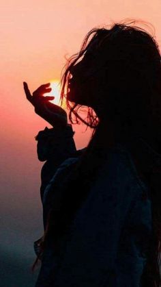 the silhouette of a woman holding her hand up to the sun