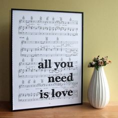 a white vase with flowers sitting next to a framed sheet music print on top of a wooden table