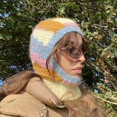 a woman wearing a multicolored knitted beanie hat and scarf in front of trees