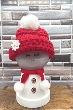 a small snowman with a red hat and scarf on it's head sitting on a table