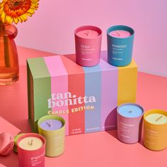 several candles are sitting in front of a box on a pink surface next to a sunflower