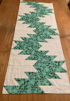 the table runner is made with green and white quilts on top of wood flooring