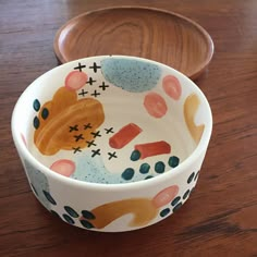 a bowl with an animal design on it sitting on a table next to a wooden spoon