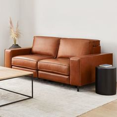 a brown leather couch sitting on top of a white rug next to a wooden table