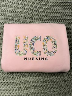 a pink purse with the word uco on it sitting on top of a green blanket