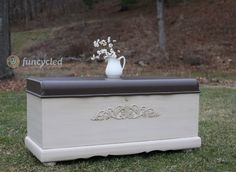 a white vase with flowers sitting on top of a wooden box in the grass next to a tree