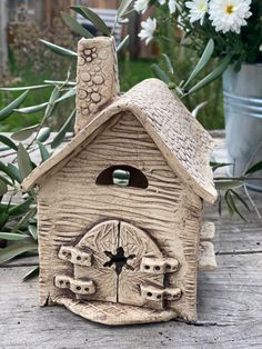 a small bird house sitting on top of a wooden table next to flowers and potted plants