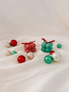 several ornaments are laying on a white sheet with red and green balls in the foreground