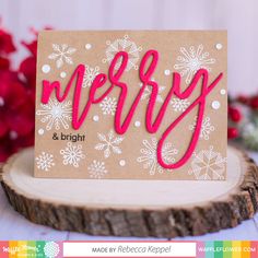 a card with the word merry and snowflakes on it, sitting on top of a piece of wood