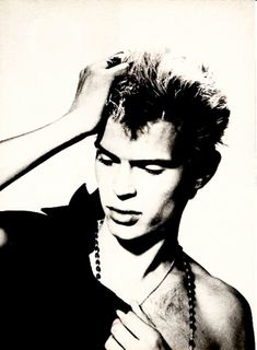 black and white photograph of a young man with his hands on his head, wearing a beaded necklace