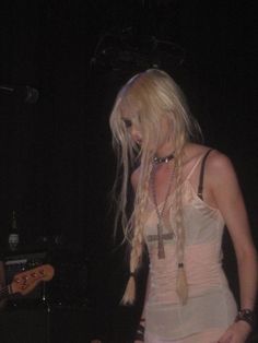 a woman with long blonde hair standing in front of a guitar and wearing a white dress