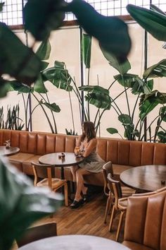 a woman sitting at a table in a restaurant with lots of plants on the walls