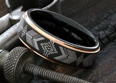 a black and gold wedding band with an arrow pattern on it sitting next to two screws