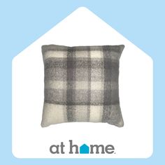 a gray and white plaid pillow sitting on top of a blue background with the at home logo