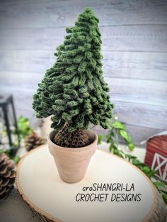 a small pine tree sitting on top of a wooden table next to a sign that says greshngrila crochet designs