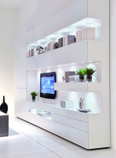 a white living room with a television on the wall and some plants in vases