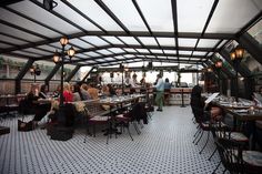 people sitting at tables in a restaurant with lots of lights on the ceiling and tiled floor