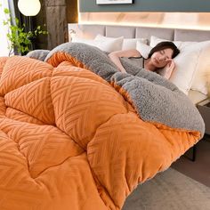 a woman laying on top of an orange comforter in a bed next to a window