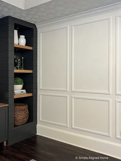 an empty room with white walls and wooden shelves on either side of the wall is a black cabinet