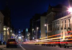 a city street at night with cars driving down the road and buildings on both sides