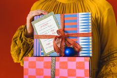 a woman holding a pink and blue gift box with a red bow on it's side