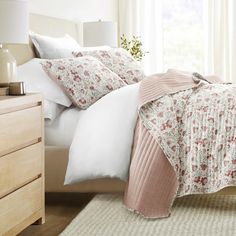 a bed with white and pink comforters on top of it next to a window