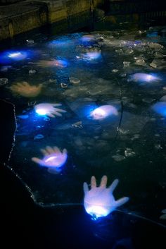 glowing hands floating in the water at night with blue lights on their palms and fingers