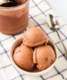 three scoops of chocolate ice cream in a bowl next to a spoon on a checkered cloth