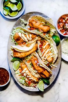 fish tacos with slaw, limes and salsa on a plate next to other dishes