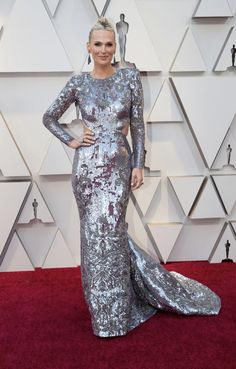 a woman in a silver gown on the red carpet at an oscars event with her hands on her hips