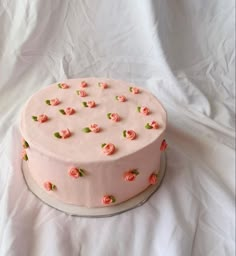 a cake with pink frosting and flowers on it sitting on a white tablecloth