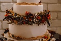 a three tiered white wedding cake decorated with dried flowers and leaves on a wooden table