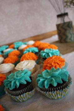 cupcakes with blue, orange and white frosting are arranged on a table