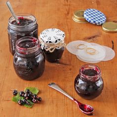 several jars of jam sit on a table with spoons and paper doily next to them