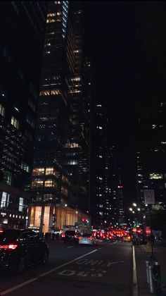 a city street at night filled with lots of traffic and tall buildings in the background